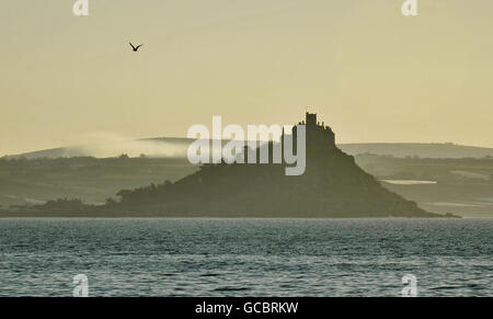 Mist flows over the hills behind St Michael's Mount, Cornwall in the early approaching Spring morning. Stock Photo