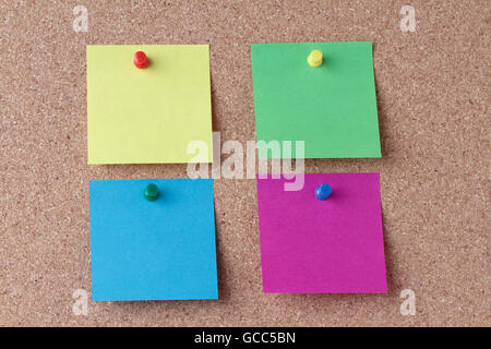 four colored notes with colored push pins on a cork board Stock Photo