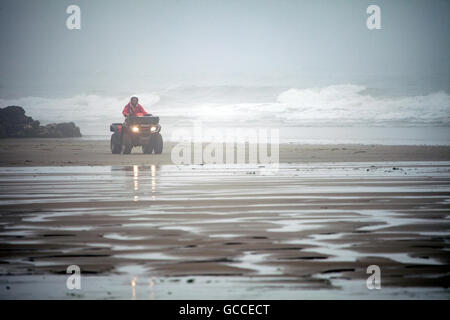 Summer fog on Whitsand Bay, Cornwall, UK as a RNLI guard drives along the beach on a quad bike Stock Photo
