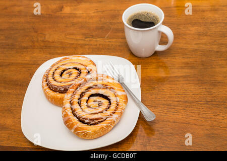 Two fresh baked cinnamon rolls on a white plate and wood table Stock Photo