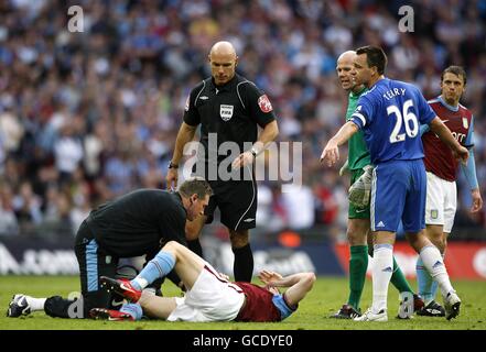 Referee Howard Webb (centre) looks on as Aston Villa's James Milner (floor) is treated on the pitch after a foul by Chelsea's John Terry (right) Stock Photo