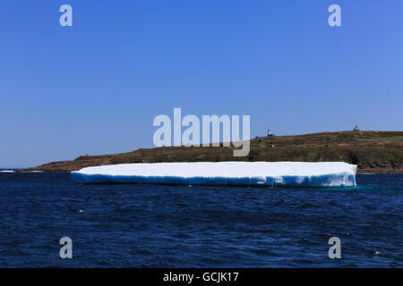 Pan-shaped iceberg near Cape Spear, Newfoundland and Labrador, Canada. The lighthouse and buildings are in the background. Stock Photo