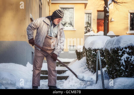 Elderly senior man shovels snow from sidewalk Stock Photo