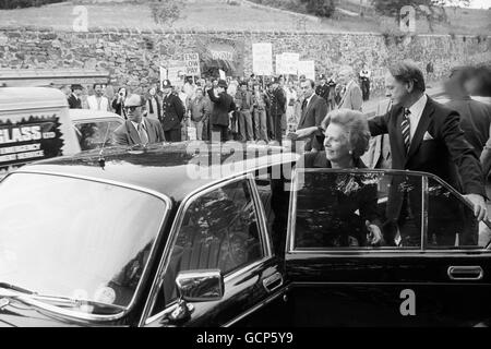 Margaret Thatcher gets into her limousine in Bristol after visiting a market garden run by the Youth Opportunities Programme at Rownham Hill, Bristol. In the background, a group of protesters demonstrate against the lack of proper jobs for the young in the area. Stock Photo