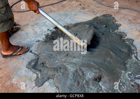 A man using a hoe to smooth cement on a sidewalk in Chork Village, Cambodia. Stock Photo