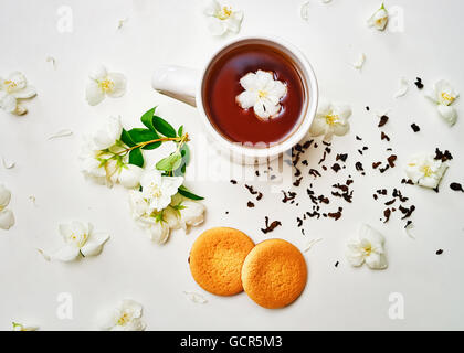 Tea cup with dried leaves and fresh fragrant Jasmine flower and biscuits on white background. Top view Stock Photo