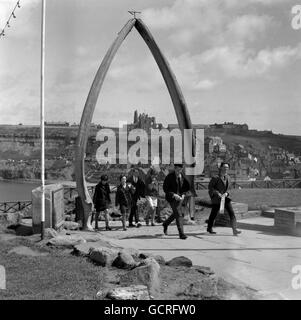 A whale's jawbone forms the graceful arch through which these holidaymakers stroll at Whitby, Yorkshire. Framed in it is the historic Whitby Abbey, across the harbour. The bone, presented by a Norwegian to the town in 1963, commemorates Whitby's past as a whaling centre, and replaced a far older whalebone arch that is now in the local museum. Whitby was a whaling port from 1753 to 1833. Stock Photo