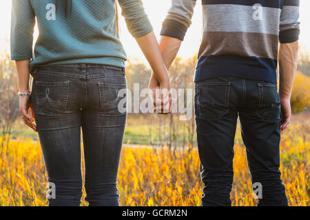 A young couple enjoying quality time together outdoors in a park in autumn and holding hands in the warmth of the sunlight during the early evening Stock Photo