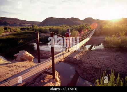 Female hiker crossing footbridge at sunset; southern Utah desert; USA Stock Photo