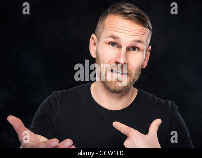 Young man in a misunderstanding on dark background. Stock Photo