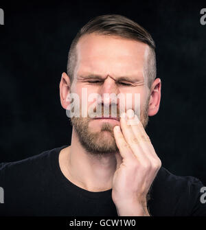 Toothache. Portrait of a man with face closed by hand. on dark background. Stock Photo