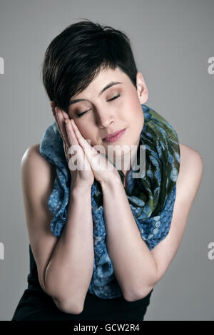 Cute pretty short hair woman pretending to sleep wearing colorful kerchief over gray studio background. Stock Photo