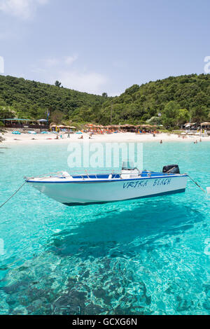 Vrika Beach, AntiPaxos, Greece - small boat moored in the clear turquoise waters of Vrika Bay looking towards beach tavernas Stock Photo