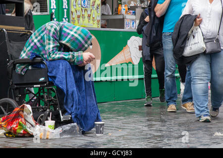 People & passers-by walking past disabled homeless beggar in a wheelchair on the streets of Liverpool, Merseyside, UK Stock Photo