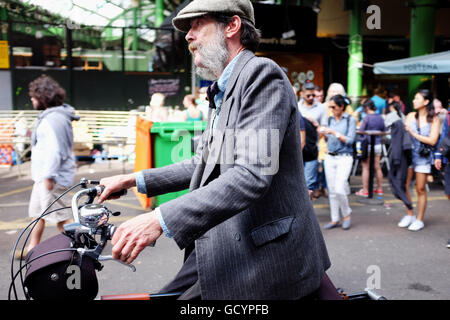 Mature man with large handlebar sideburns wearing grey jacket and cap on a bicycle Stock Photo