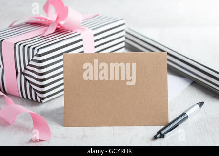 Empty greeting kraft card with pen. Wrapped gift and wrapping paper roll in the background. Stock Photo