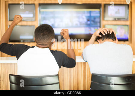 Closeup portrait, two men watching a sports game on tv.  One guy rejoices, other guy feels terrible. Team spirit concept Stock Photo