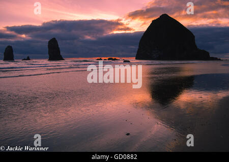 Haystack Rock and 'The Needles' reflected in the wet sand at sunset at Cannon Beach, Oregon Stock Photo