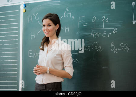 Young happy female teacher with arms crossed standing against green board Stock Photo