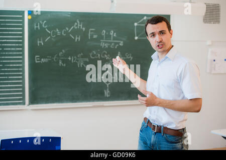 Young teacher near chalkboard in school classroom talking to class Stock Photo