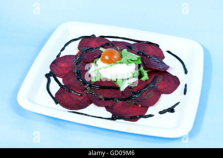 Modern food on a white plate and blue background - Thin slices of beetroot with goat cheese and balsamic reduction Stock Photo