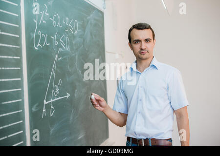 Young male teacher or student holding chalk writing on chalkboard in classroom Stock Photo