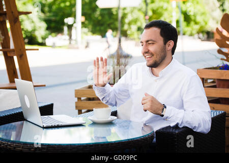 Work and relax. Online conference. Businessman dressed in shirt working with laptop, talking by skype at the park cafe outdoors Stock Photo