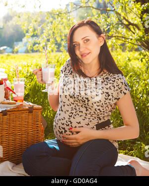 Portrait of beautiful pregnant woman drinking milk shake at picnic in the spring park Stock Photo