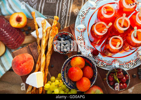 Picnic on the beach at sunset with fruits and juices in the style of boho Stock Photo