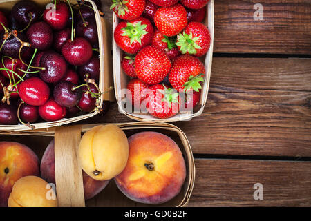 Fresh ripe summer berries and fruits (peaches, apricots, cherry, strawberry) in baskets, top view Stock Photo