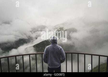 View from behind of a man standing at view point looking to beautiful landscape with foggy mountains in the distance Stock Photo