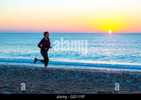 Young Woman jogging on Beach along Sea Surf at Sunrise Stock Photo