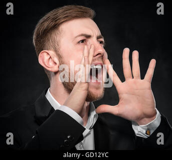 Businessman in black suit shouts lifting his hands up. on a dark background. Stock Photo