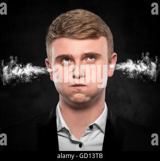 Stressful man with smoke or fume coming out from his ears on dark background. Stock Photo