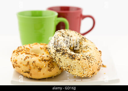 Two bagels on white plate with red and green mugs behind.  Selective focus on breakfast bread. Stock Photo