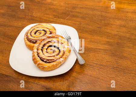 Two fresh baked cinnamon rolls on a white plate and wood table Stock Photo