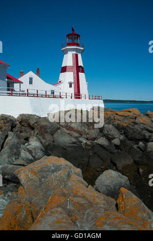 Head Harbor lighthouse, with its unique red cross painted on the tower, over rocky shore during low tide. Stock Photo