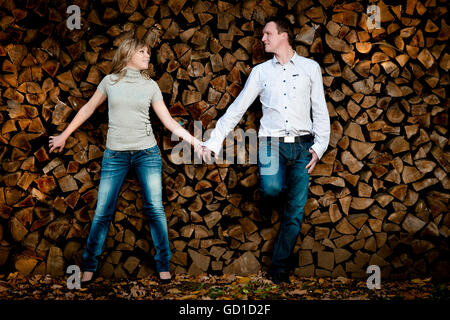 Young couple, hand in hand, leaning against a wood pile Stock Photo