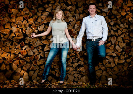 Young couple, hand in hand, leaning against a wood pile Stock Photo