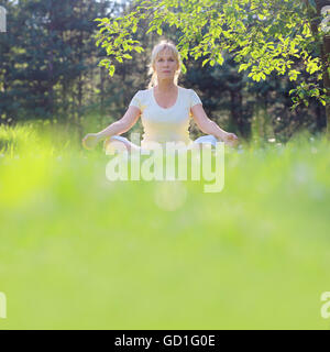 Beautiful mature woman in lotus yoga position in summer park Stock Photo