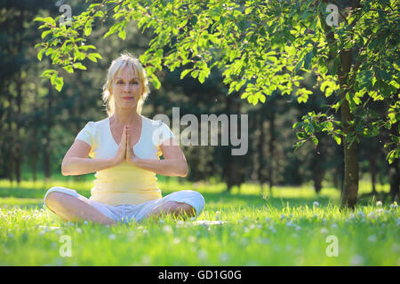 Beautiful mature woman in lotus yoga position in summer park Stock Photo