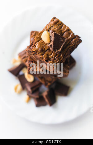 Brownies with peanuts and dark chocolate stacked on white dessert plate. Selective focus Stock Photo