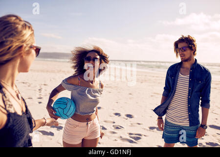 Portrait of young african woman on the beach holding a ball with friends standing by. Group of friends at the sea shore on a sum Stock Photo