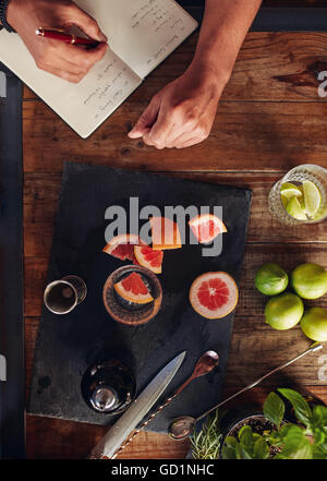 Set of bar accessories and ingredients for making a cocktail arranged on a wooden table with bartender taking notes. Stock Photo