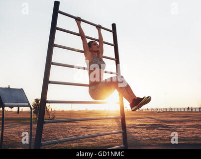 Portrait of strong young woman hanging on wall bars with her legs up. fitness woman performing hanging leg raises on outdoor. Stock Photo