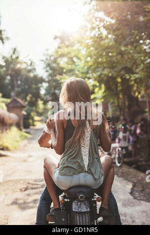 Rear view shot of young couple riding motorcycle through a village. Young female sitting on back of her boyfriend riding bike. Stock Photo