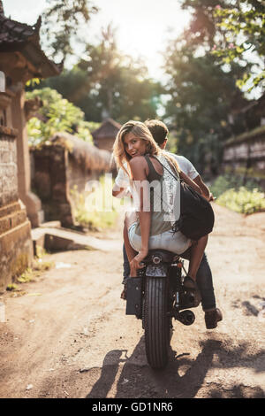 Rear view shot of young couple riding motorcycle on rural road. Beautiful young female sitting on back of her boyfriend riding b Stock Photo