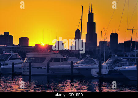 The setting sun creates a glow in the sky and into Chicago's Burnham Harbor as it dips toward the horizon and  Willis Tower. Chicago, Illinois, USA. Stock Photo