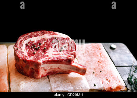 Bone In Rib Eye row Steak on pieces of salt on a wooden board. Stock image Stock Photo