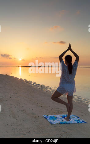 Woman practising yoga at sunrise, Rasdhoo Island, Northern Ari Atoll, Maldives, Indian Ocean, Asia Stock Photo